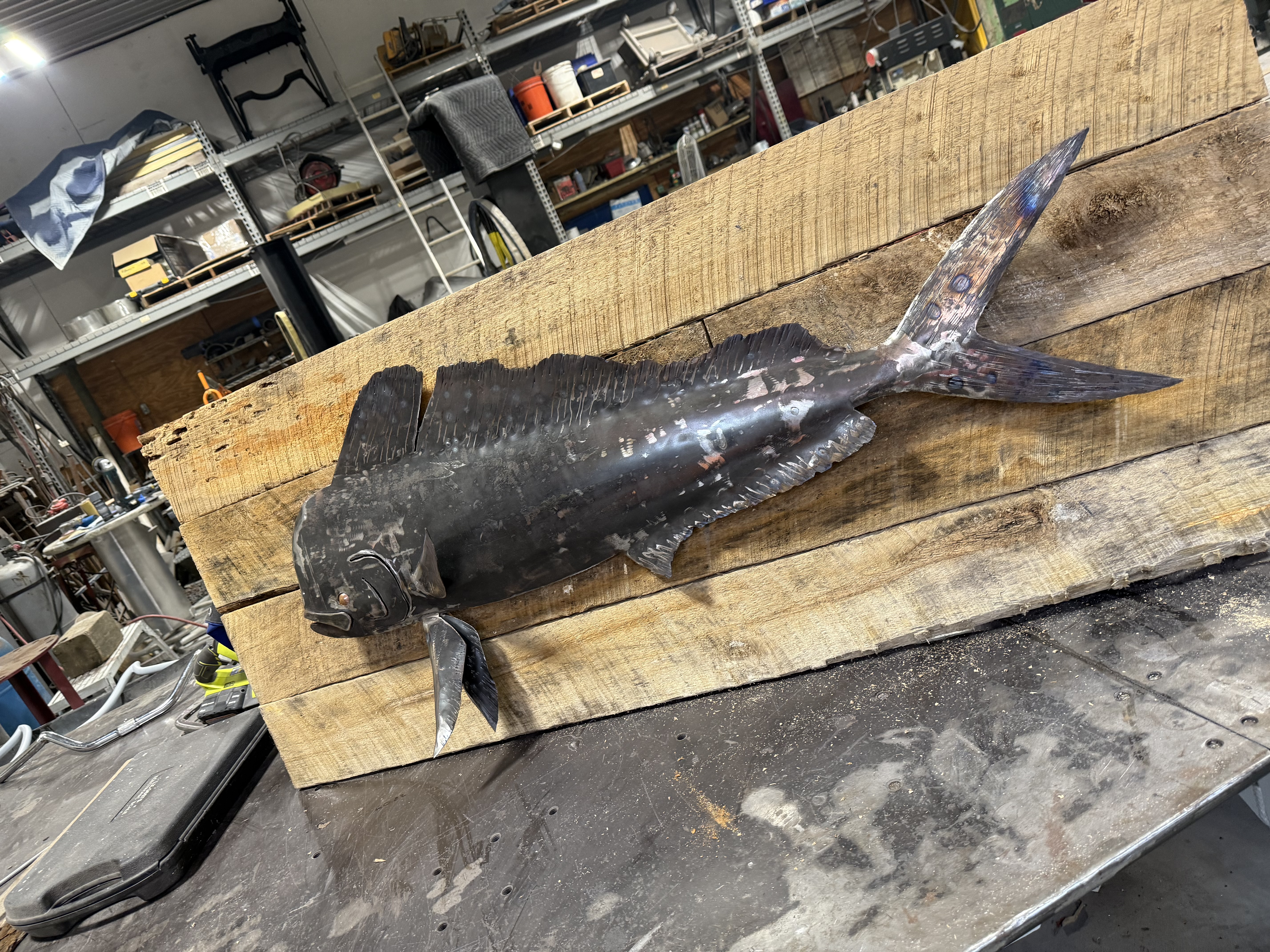 Steel mahi-mahi sculpture resting on a workshop pallet